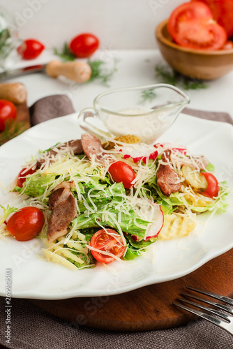Salad with roasted meat, radish, lettuce, cherry tomatoes, cheese, and pickled cucumbers. Cafe menu on a wooden background in warm colors.