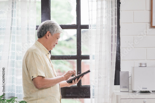 Wallpaper Mural Asian elderly man using tablet checking social media near window in living room at home. Lifestyle senior men at home concept. Torontodigital.ca
