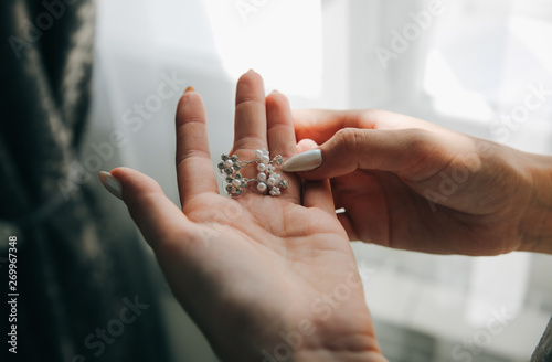 Beautiful bride holding in her hands the earrings. Woman with jewelry.