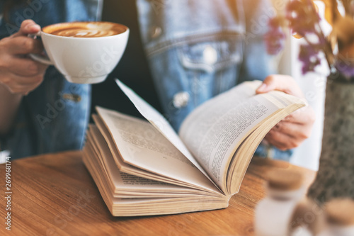 Fototapeta Naklejka Na Ścianę i Meble -  Closeup image of a woman holding and reading a vintage novel book while drinking coffee