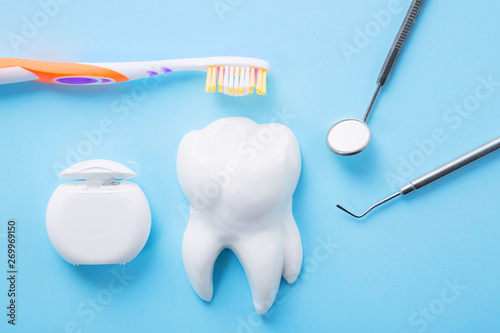 Dental health and teethcare concept. Professional steel dental instrument with a mirror near white tooth model, toothbrush and dental floss on light blue background. © Nikolay N. Antonov