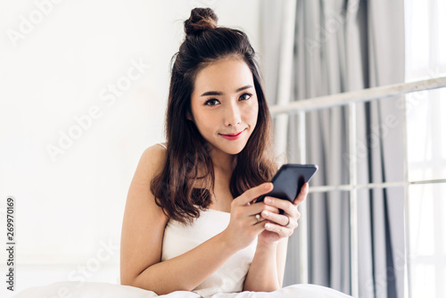 Happy woman relaxing using and talking by smartphone on the bed at home.technology and communication concept