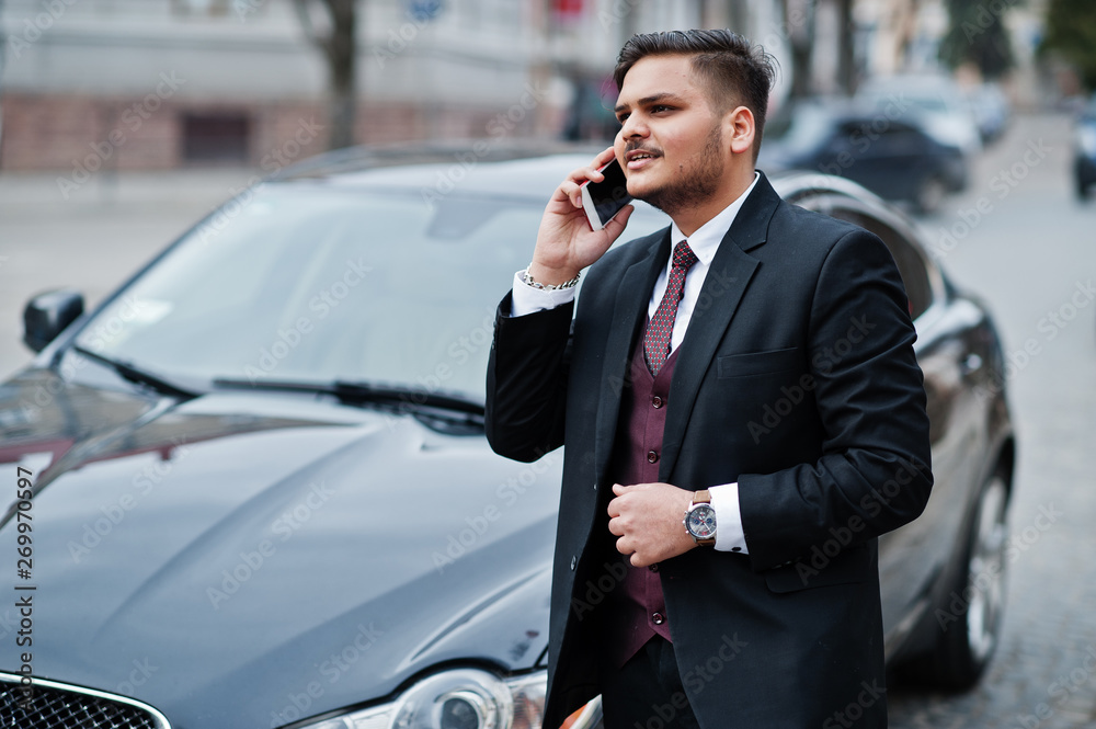 Stylish indian businessman in formal wear with mobile phone standing against black business car on street of city. Talk on cellphone. Stylish indian businessman in formal wear with mobile phone standing against black business car on street of city. Talk on cellphone.