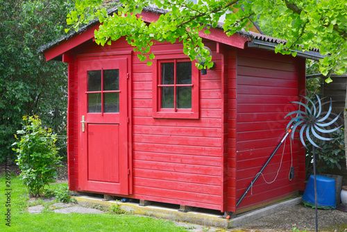 Rot gestrichenes Gartenhaus unter einem Baum in einer häuslichen Gartenanlage,  photo