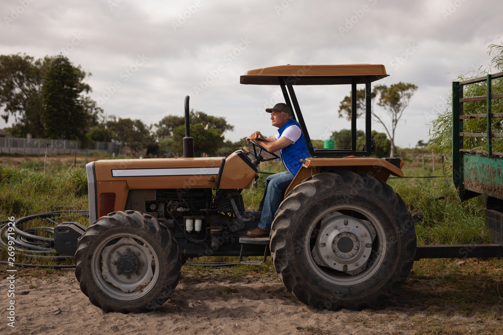 Senior male farmer driving tractor in farm Senior male farmer driving tractor in farm