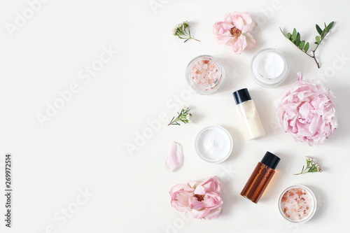 Styled beauty composition. Skin cream jar, tonicum bottle, roses, peony flower and Himalayan salt on white table background. Organic cosmetics, spa concept. Empty space, flat lay, top view.