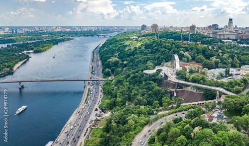 Aerial drone view of new pedestrian cycling park bridge construction, Dnieper river, hills, parks and Kyiv cityscape from above, city of Kiev skyline, Ukraine
