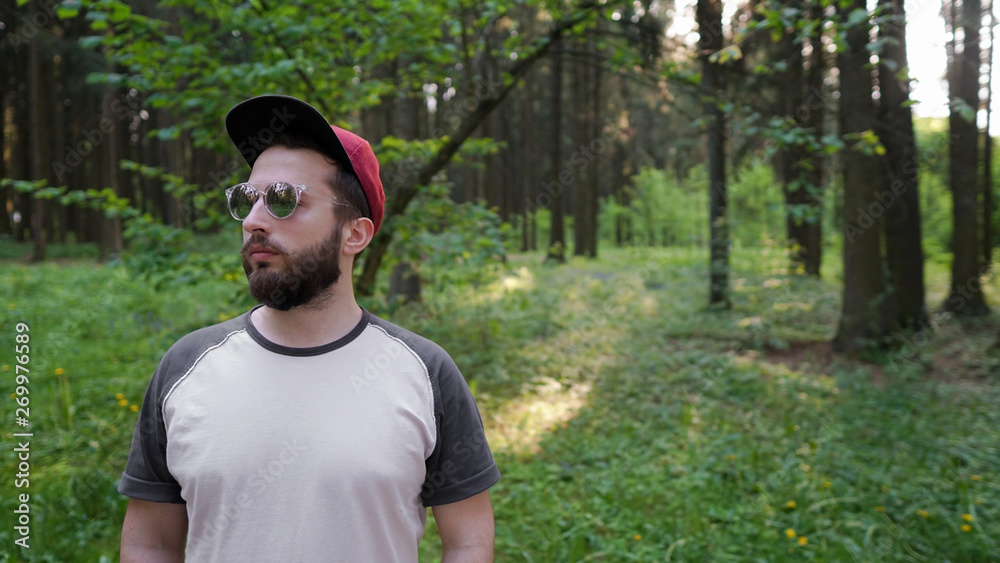 Young man with beard in sunglasses, hipster traveler in the sunny forest. Adventure, vacation, wanderlust, nature. Young man with beard in sunglasses, hipster traveler in the sunny forest. Adventure, vacation, wanderlust, nature.