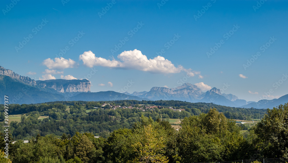 Beautiful summer panorama of the French Alps and a green hill with a village in the Auvergne Rhone Alps region.