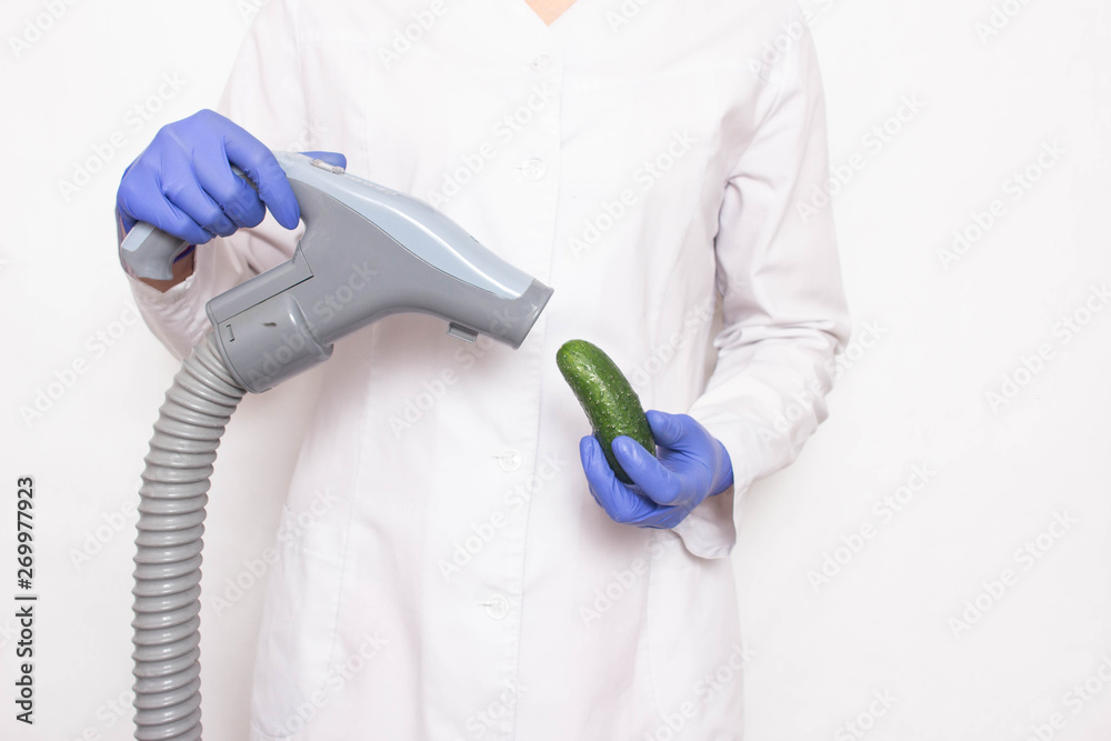 Doctor holds a cucumber near the vacuum cleaner on a white background, the  concept of increasing penis in men with a vacuum pump, increasing the  length of the male organ Stock Photo
