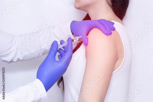 Doctor makes an injection of blockade of chondroprotector and anti-inflammatory drug in the girl's sore shoulder, white background, close-up, ozone therapy