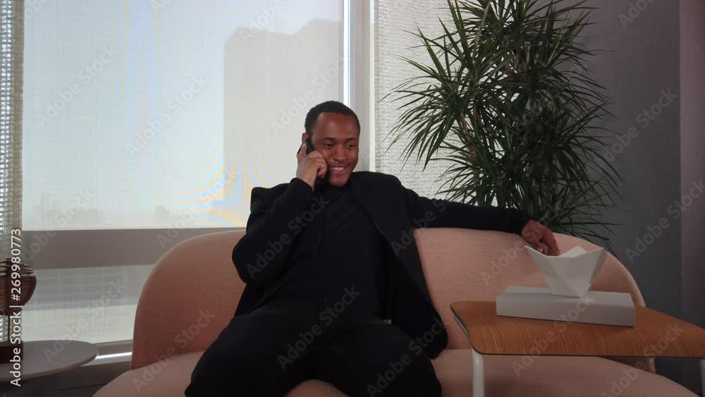 Happy African American Man talking on cell phone while sitting on sofa. Happy African American Man talking on cell phone while sitting on sofa.