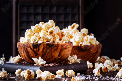 Salted popcorn in a wooden bowl, unhealthy food, dark wooden kitchen table background, selective focus