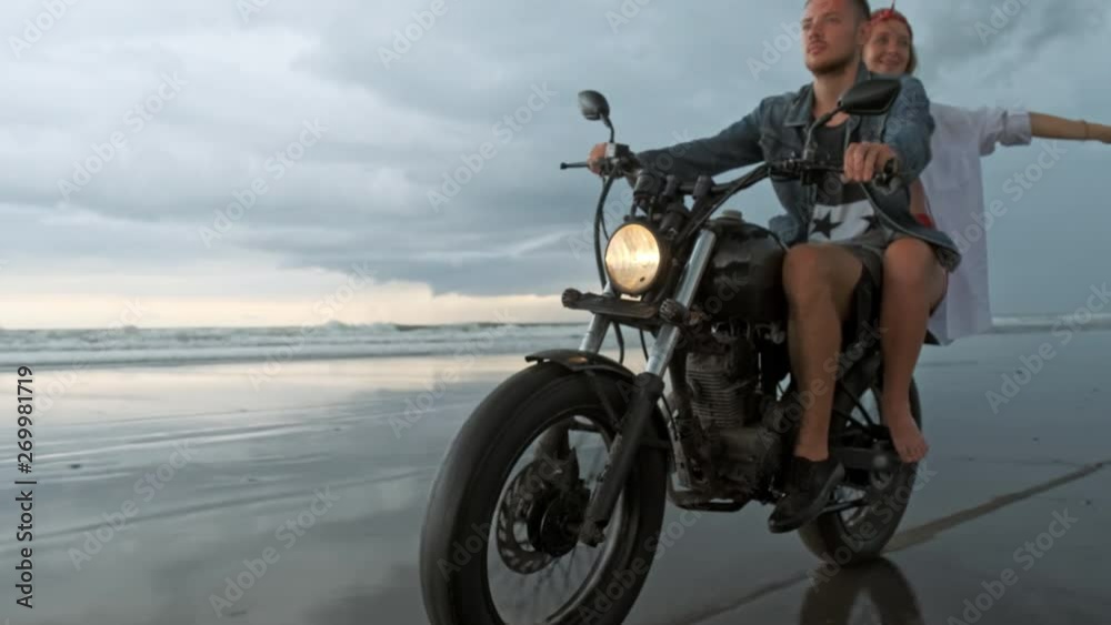 Young beautiful couple hipsters riding retro motorcycle on the beach, outdoor portrait, riding guy and girl, travel together, ocean, sea Young beautiful couple hipsters riding retro motorcycle on the beach, outdoor portrait, riding guy and girl, travel together, ocean, sea