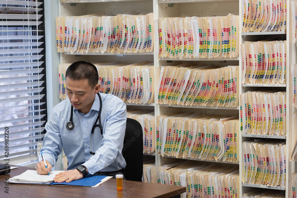 Yong asain male doctor prescribing medicine on report in the clinic Yong asain male doctor prescribing medicine on report in the clinic