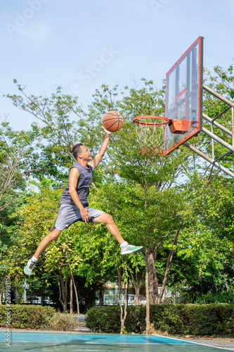 Basketball in hand man jumping Throw a basketball hoop Background  tree in park. © Nueng