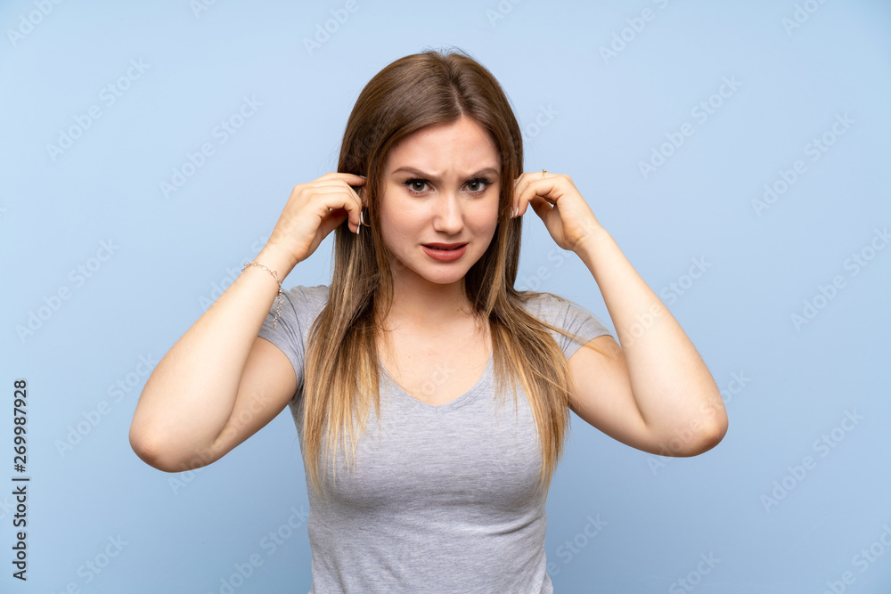 Teenager girl over isolated blue wall frustrated and covering ears Teenager girl over isolated blue wall frustrated and covering ears