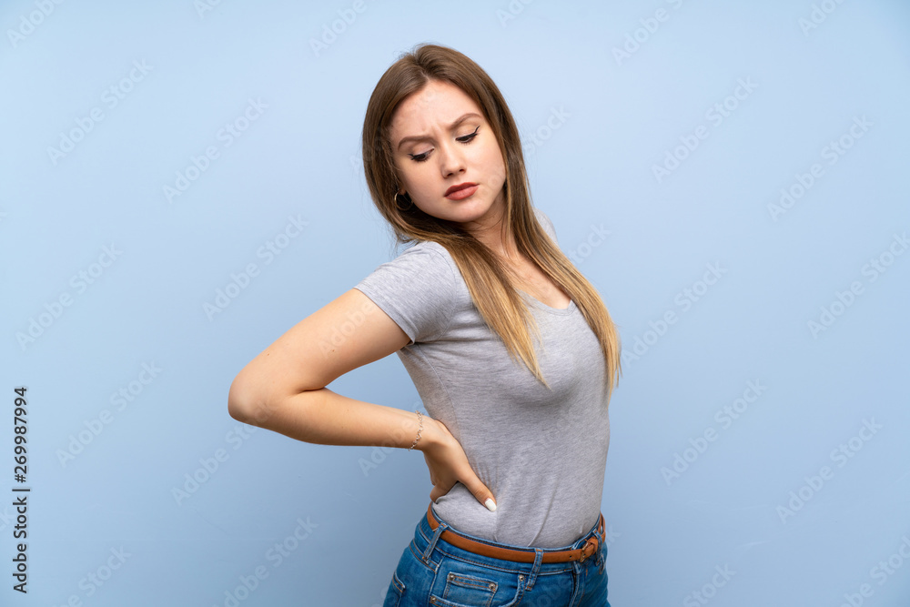 Teenager girl over isolated blue wall suffering from backache for having made an effort Teenager girl over isolated blue wall suffering from backache for having made an effort