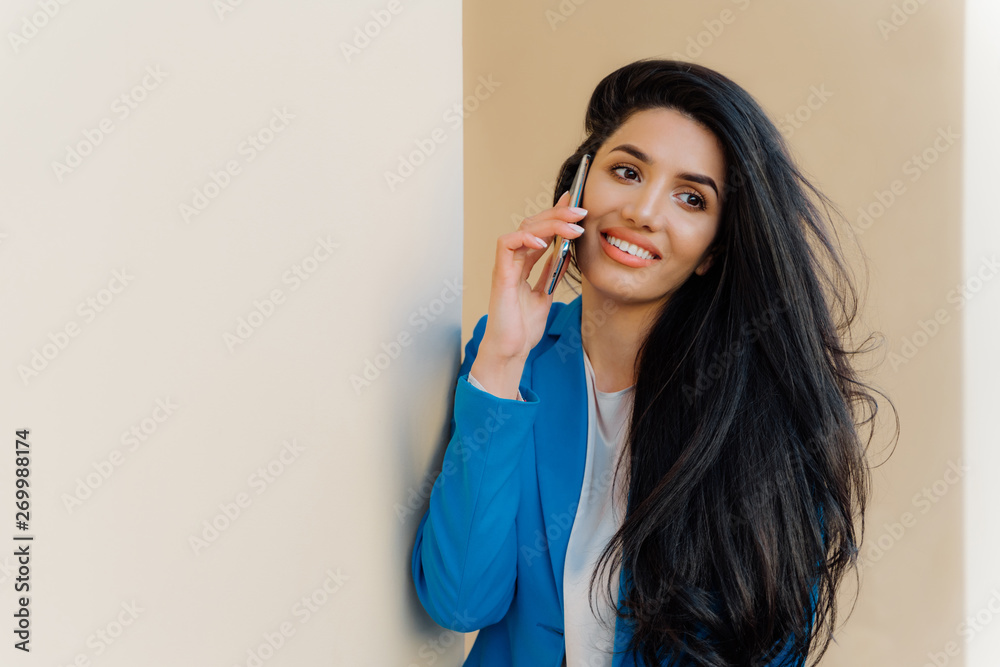 Happy young female student talks via cell phone after exam, shares her success. Brunette woman entrepreneur enjoys phone conversation, looks aside gladfully, wears formal outfit, communicates Happy young female student talks via cell phone after exam, shares her success. Brunette woman entrepreneur enjoys phone conversation, looks aside gladfully, wears formal outfit, communicates