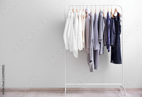 Rack with stylish clothes near light wall