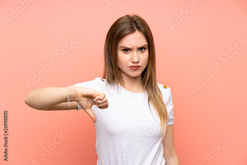 Teenager girl over isolated pink wall showing thumb down sign