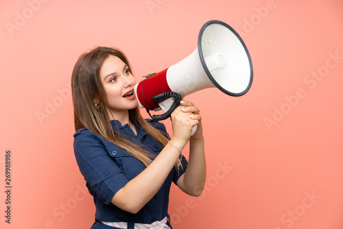 Teenager girl over isolated pink background shouting through a megaphone