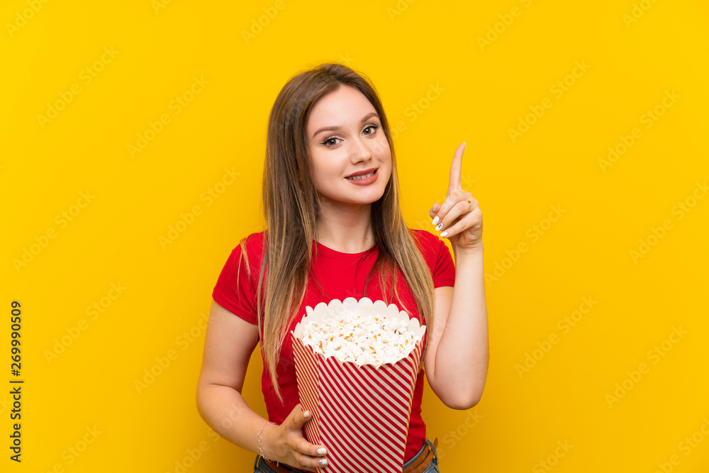 Young woman with popcorns over pink wall pointing up a great idea Young woman with popcorns over pink wall pointing up a great idea