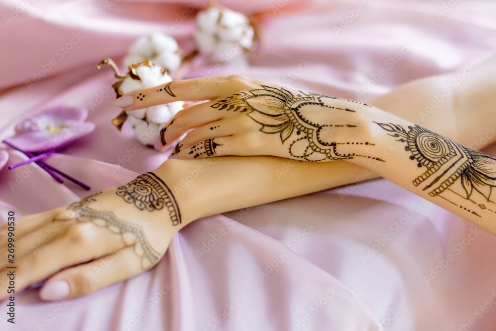 Closeup slender female wrists painted with traditional indian oriental  mehndi ornaments. Womens hands decorated with henna tattoo. Light pink  fabric with folds, cotton flowers on background. Stock Photo | Adobe Stock