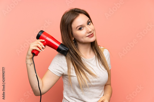 Teenager girl over pink background with hair dryer