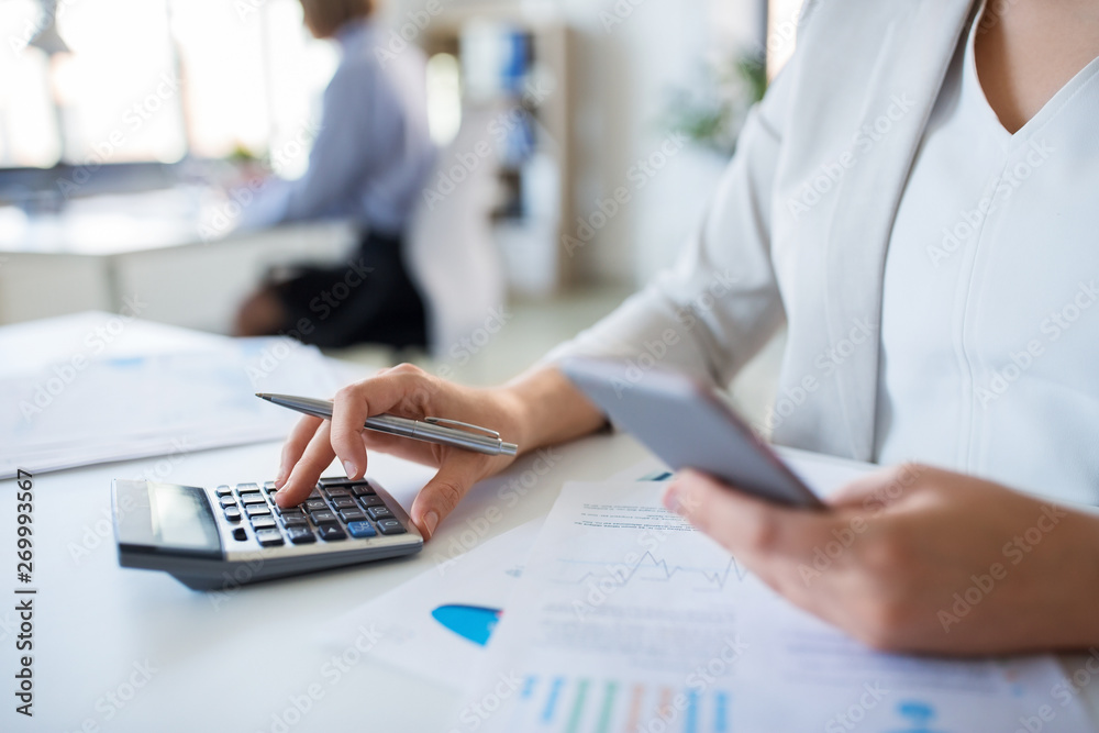 Fototapeta premium business and people concept - businesswoman with calculator, smartphone and papers working at office
