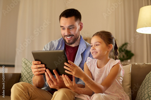 family, fatherhood and technology concept - happy father and little daughter with tablet pc computer at home in evening