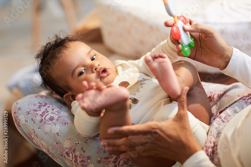 Close-up of curious cute baby with ratty hair lying on mothers knees and touching own foot, mother playing with baby