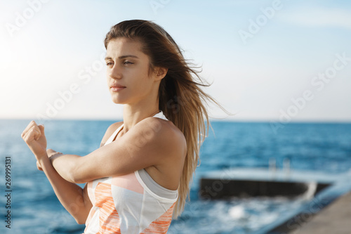 Girl set up goal, keep body fit, stretching arms, doing jogging warm-up exercises looking determined, focused workout, standing near sea enjoying quay air during everyday morning fitness running