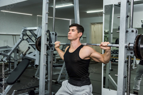 Athletic man lifting dumbbell in gym on shoulders