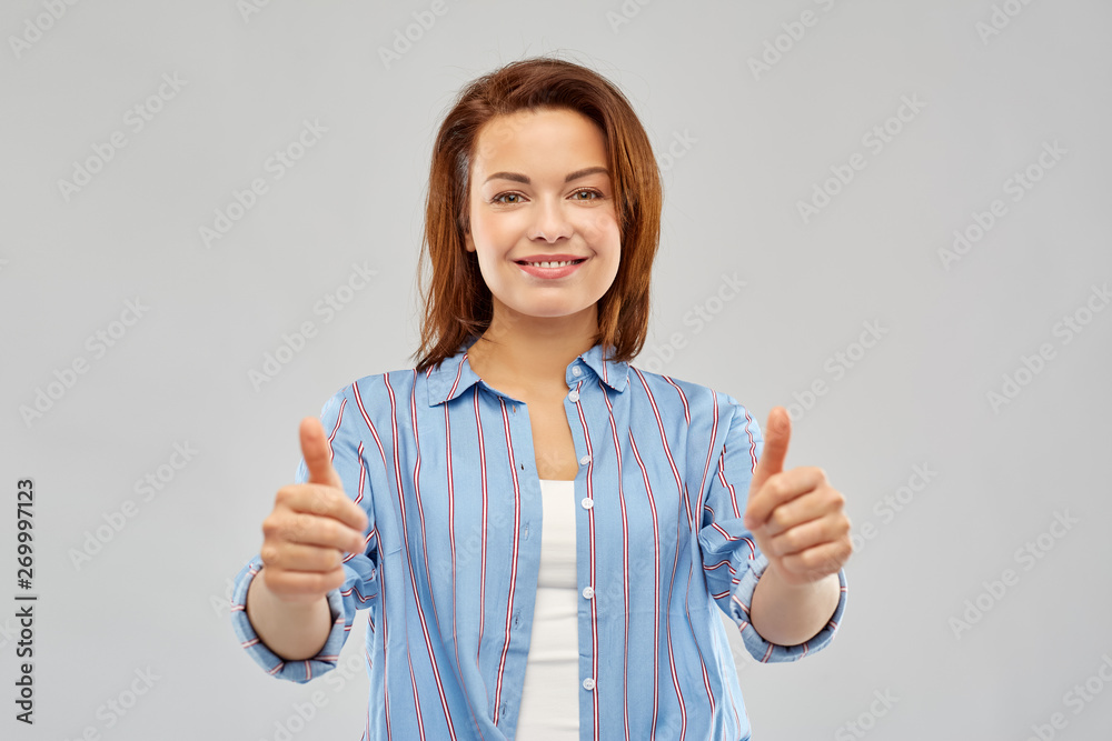 gesture and people concept - happy smiling young woman in striped shirt showing thumbs up over grey background gesture and people concept - happy smiling young woman in striped shirt showing thumbs up over grey background