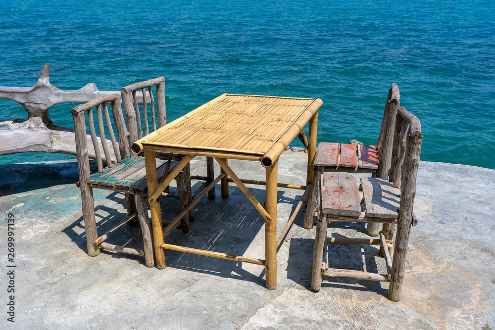 Bamboo table and wooden chairs in empty cafe next to sea water in tropical beach . Island Koh Phangan, Thailand