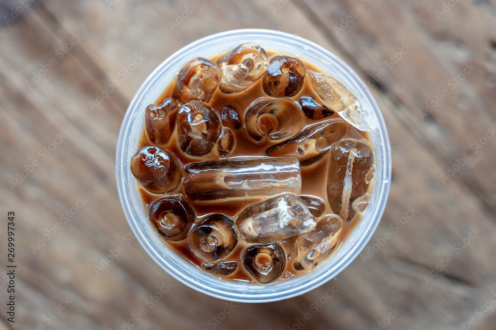Iced coffee or latte top view on wooden background. Black coffee with ice in plastic glass, closeup Iced coffee or latte top view on wooden background. Black coffee with ice in plastic glass, closeup