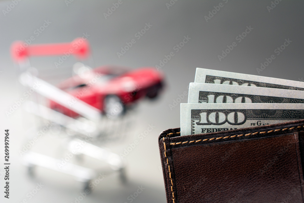 leather wallet with dollars blurred red car shopping trolley on the background. cheap used cars concept leather wallet with dollars blurred red car shopping trolley on the background. cheap used cars concept