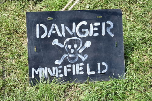 Tableau sur toile Danger minefield, black sign with white skull and crossbones on a grass, closeup