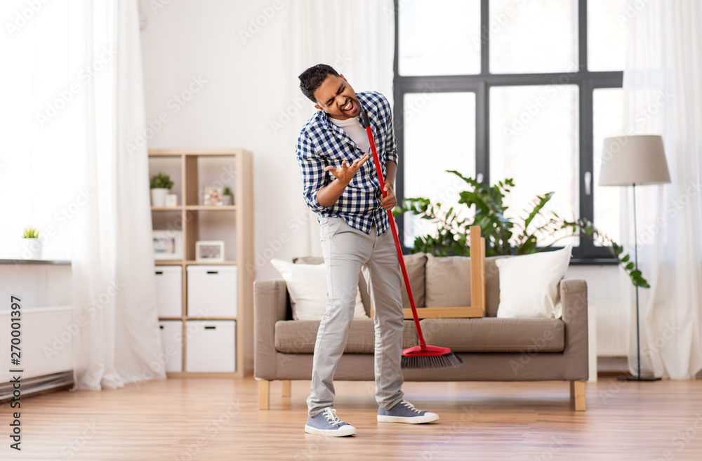 cleaning, housework and housekeeping concept - indian man with broom sweeping floor and singing at home cleaning, housework and housekeeping concept - indian man with broom sweeping floor and singing at home