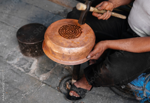 A craftsman is engaged in chasing a copper plate on the street