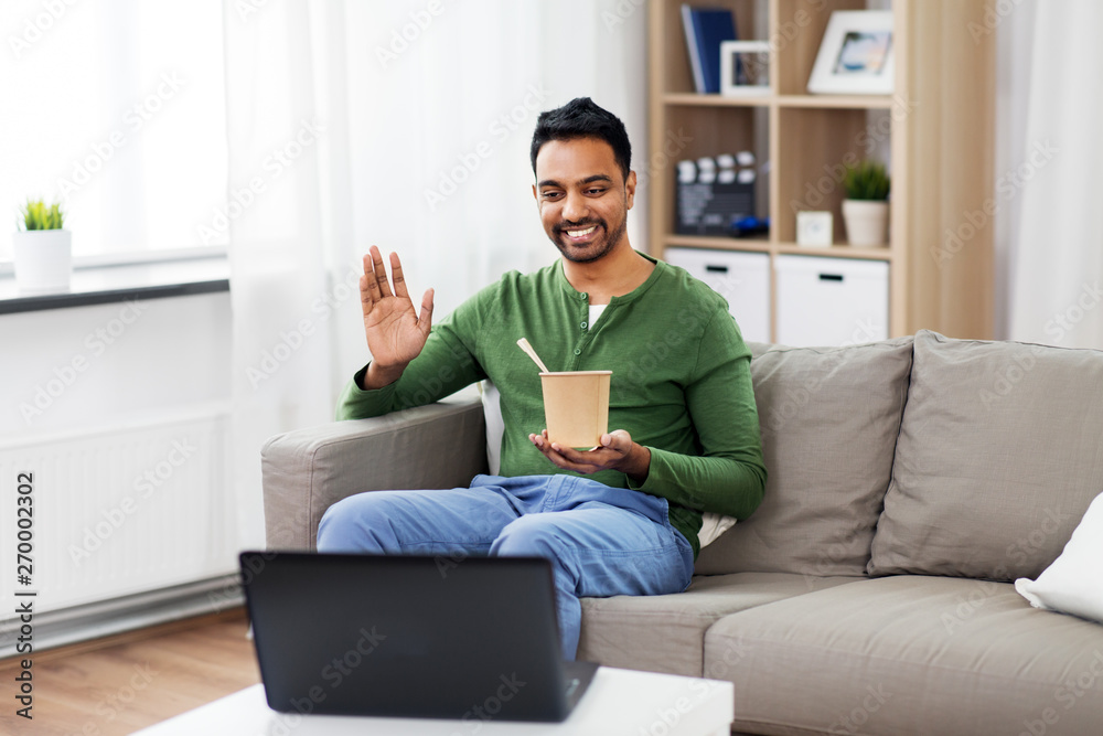 consumption and people concept - smiling indian man having video call on laptop computer, eating takeaway food and waving hand at home consumption and people concept - smiling indian man having video call on laptop computer, eating takeaway food and waving hand at home