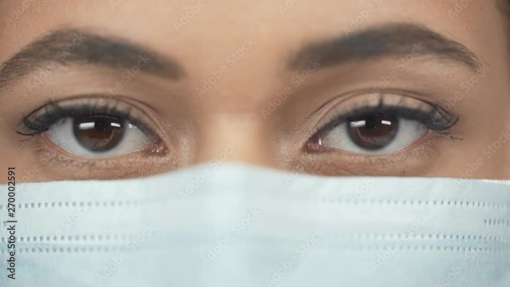 close up view of african american woman in medical mask blinking while looking at camera