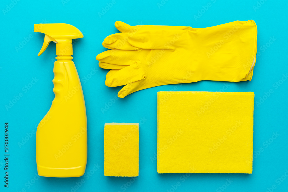 yellow cleanser in plastic container with spray, rubber protective gloves, sponge and cloths for cleaning on the turquoise blue background. flat lay image of yellow cleaning products in order