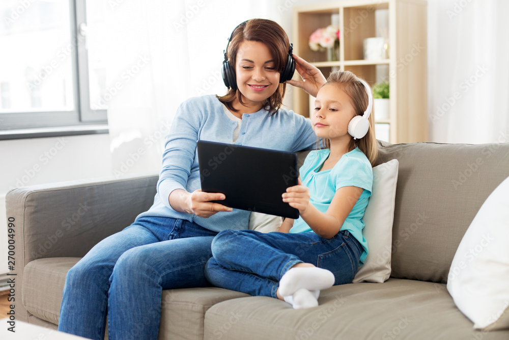 people, family and technology concept - happy mother and daughter with tablet pc computer and headphones listening to music at home people, family and technology concept - happy mother and daughter with tablet pc computer and headphones listening to music at home