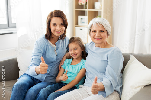 family, generation and female concept - mother, daughter and grandmother sitting on sofa and showing thumbs up