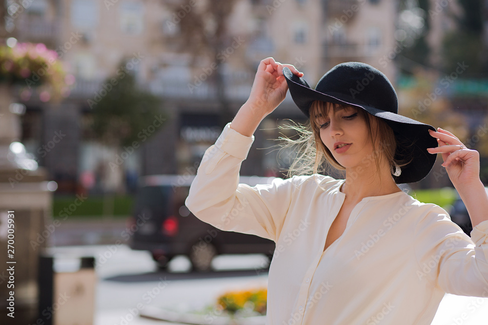 Street shot of lovely brunette model wearing white shirt and hat. Empty space