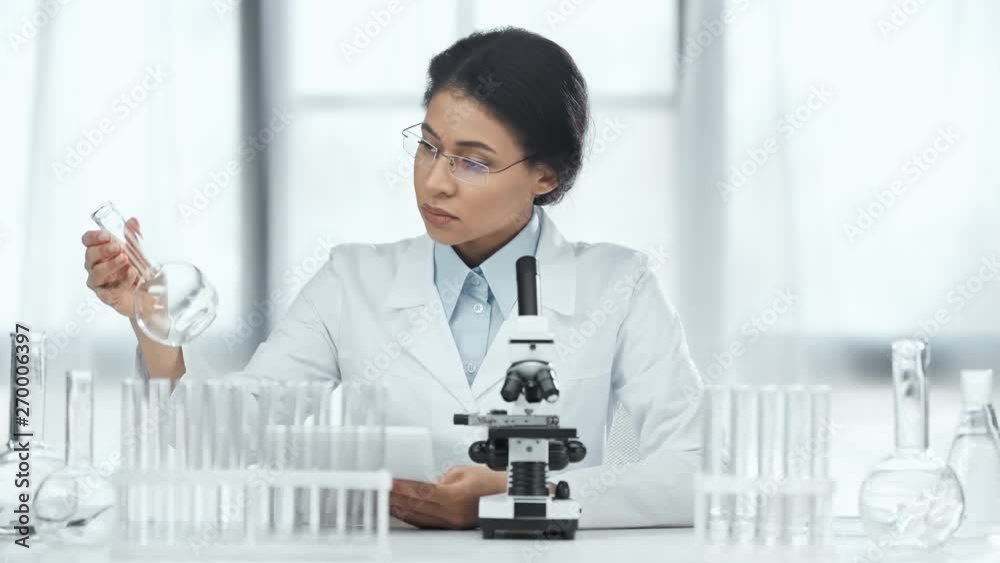 african american scientist using digital tablet and looking at glass flasks in lab african american scientist using digital tablet and looking at glass flasks in lab