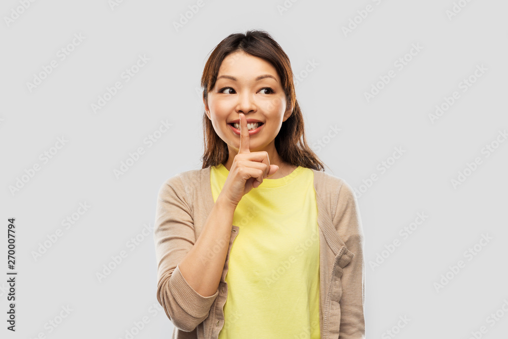 people, silence and secret concept - happy asian young woman with finger on lips over grey background people, silence and secret concept - happy asian young woman with finger on lips over grey background