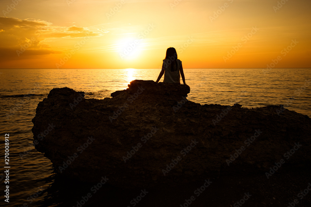 silhouette of a young girl. sits and watches the beautiful sunset on the sea.